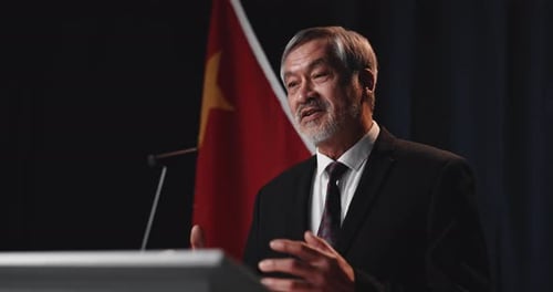 Man Giving Speech at Podium with Flag Backdrop