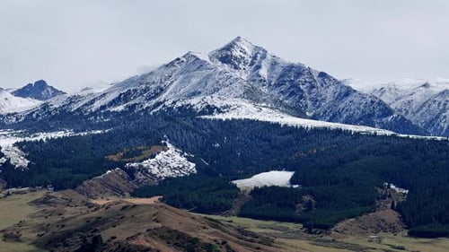 Snowcapped Mountain Peak with Conifer Forest and Snow Patches in Winter