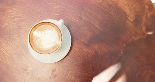 A cup of coffee with latte art sits on a wooden table in a cafe with copy space