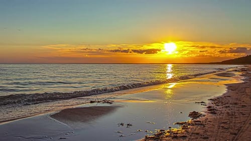 Time lapse of vibrant sunrise along coast, small waves break on sandy beach