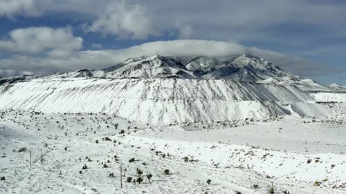 Aerial view across snow covered white high altitude mountain summit slopes. Dolly left across landsc