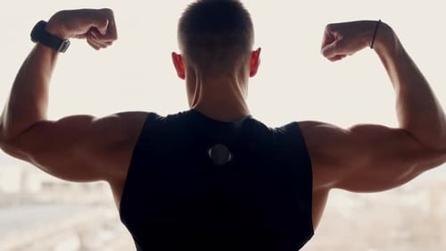 Muscular Man Flexing Biceps in Front of Window