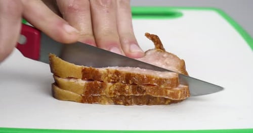 una mano corta de cerca una pechuga ahumada con un cuchillo, corta un trozo de pechuga de cerdo