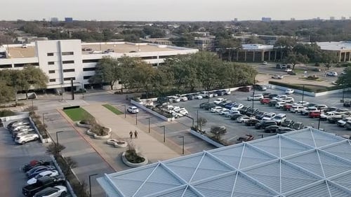 This video show a busy parking lot at an office complex with cars driving around and people walking