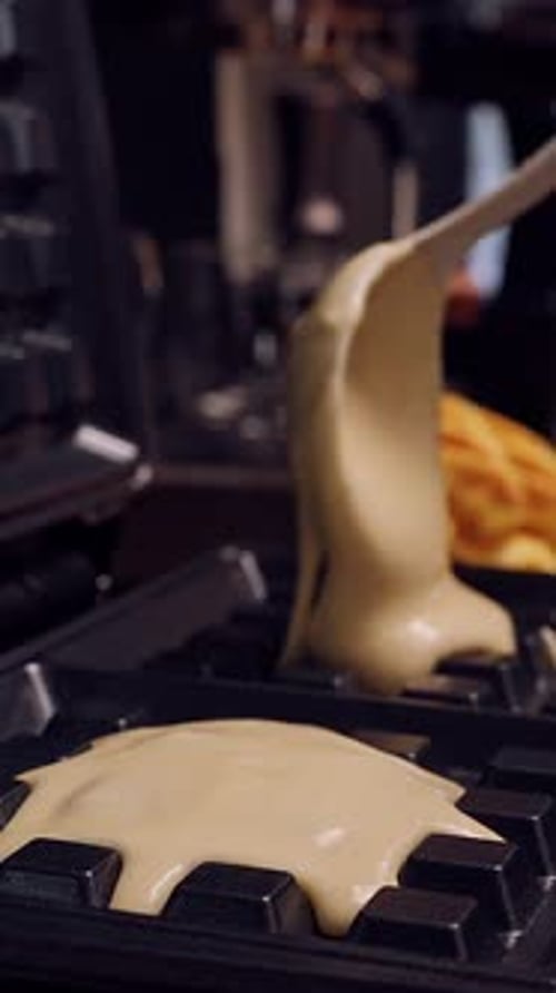Vertical video. Close Up Of Batter Being Poured Into Waffle Maker With Finished Waffles Visible