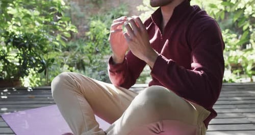 Midsection of caucasian man practicing yoga meditation on terrace in sunny nature, slow motion