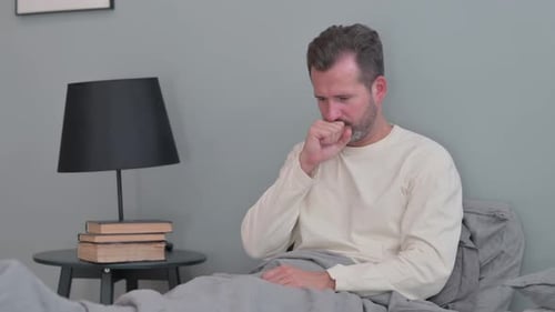 Un homme d'âge moyen qui tousse ne se sent pas bien au lit