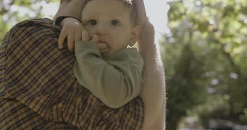 Father carrying baby boy son in park in autumn and comforting under tree in the sun
