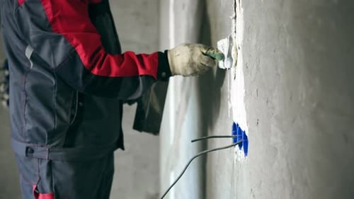 Man Plastering Wall Around Electrical Outlet in Home