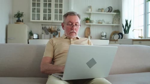 Senior Man Using Laptop on Couch Indoors