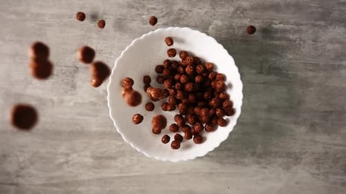 Cereal Balls Pouring into White Bowl Overhead
