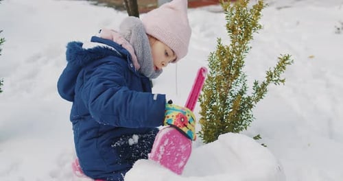 Cute Girl Builds and Plays in the Snow in the Forest
