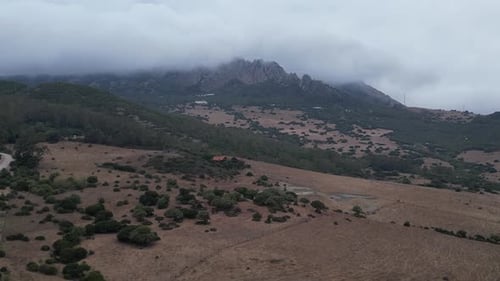 Drone rising up revealing a cloud covered rocky mountain in a Spanish countryside.