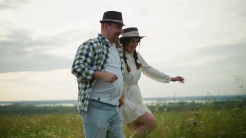 Joyful Couple Holding Hands and Running Through a Grassy Field at Sunset