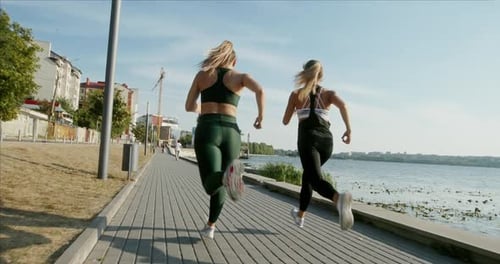 Tracking Shot of Anonymous Female Athletes Running on Paved Path Near Sea Water During Fitness