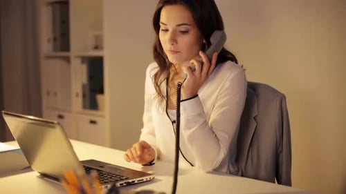 Woman working late using laptop and talking phone