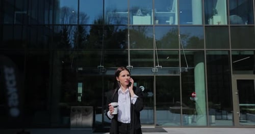 Young Successful Businesswoman in a Suit Walking Near a Modern Business District During Talking on