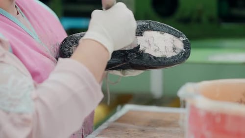 Worker applying glue to the sole of a shaped shoe in a shoemaking factory, close-up.