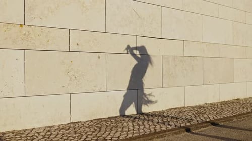 Woman's Shadow Dances Along Neutral Tiled Wall