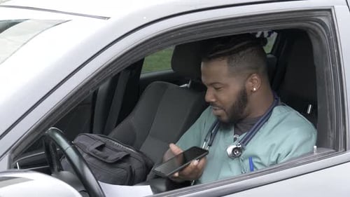 Man in Scrubs Uses Smartphone in Car