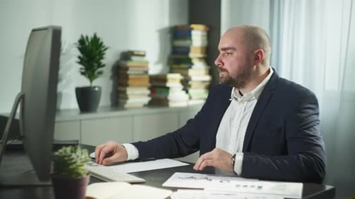 Ein Mann arbeitet zu Hause aus der Ferne an einem Computer, schreibt mit einem Stift in ein Notizbuch
