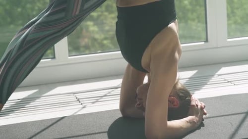 Une jeune femme portative fait des étirements et fait du yoga dans une pièce blanche remplie de lumière