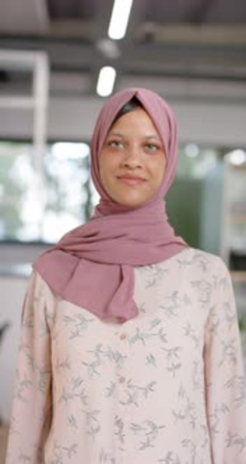 Vídeo vertical de retrato de uma empresária casual biracial feliz em hijab no escritório, câmera lenta