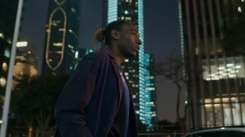 Young black man walking alone around the city at night with city lights background