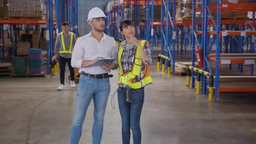 Young woman talking with manager while signature document on clipboard in the warehouse at factory.