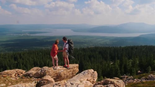 Young Man and Woman Standing on the Edge of Mountain and Raising Hands Up