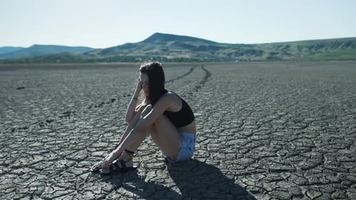 Woman Sits in a Dry, Cracked Desert