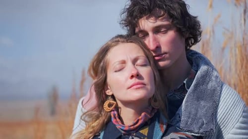 Couple romantically embraces in golden wheat field beneath clear sky.