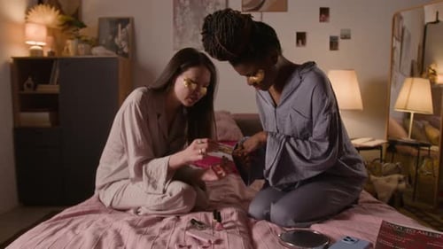 Asian Girl Giving Manicure to African American Friend at Pajama Party