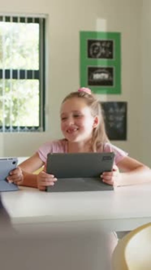 Vertical video: Pulling focus, curly child in dark top turning toward peer with tablet in class