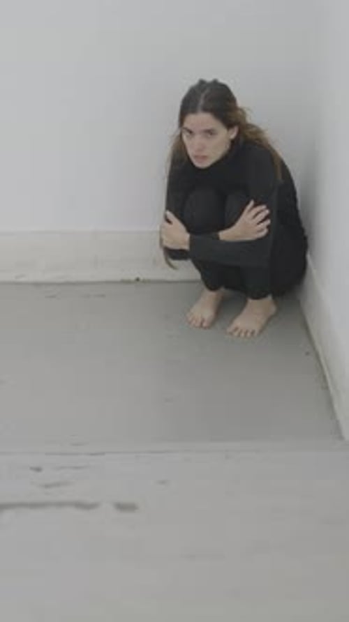 Young Woman Sits in Corner of Stairwell Looking Scared Slow Pan