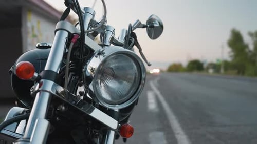 Parked Motorcycle with Passing Car and Distant Headlights on Road