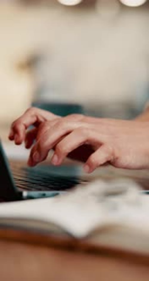 Hands Typing on Laptop Keyboard with Open Book