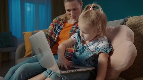 Mom Teaches Her Little Daughter to Work on a Laptop Close Up Mom and Daughter Sitting on the Sofa in