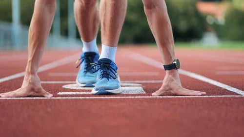 Close-up pan shot of runner at the starting position of running track