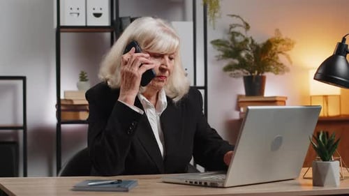 Senior Caucasian Businesswoman Operator Using Smartphone and Laptop Computer at Home Office Desk