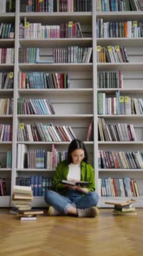 Young Woman Reads Book on Library Floor