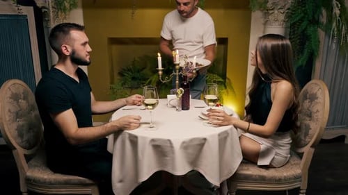 A young couple is sitting in an expensive restaurant the waiter brings dishes to the guests a date