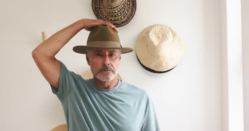 Mature man picking brown-green fedora from hat display, inspecting fit and adjusting hat on head