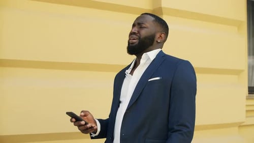 Upset man checks phone outside building, blue suit