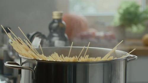 Hands Placing Bunch of Spaghetti into Pot of Boiling Water
