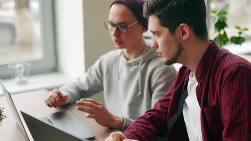 Deux collègues branchés partagent des idées sur la gestion de projets avec des ordinateurs portables dans un bureau spacieux à aire ouverte