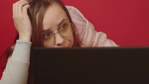 Young Woman in Glasses Works on Laptop and Scratches Head Sitting in Home Office
