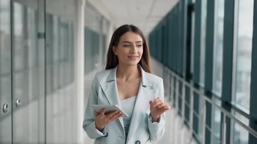 Stylish young beautiful woman in a suit walking down the hall with a tablet