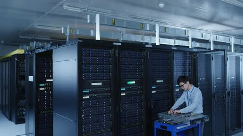 In the Modern Data Center: IT Technician Working with Server Racks, on a Pushcart Various Equipment
