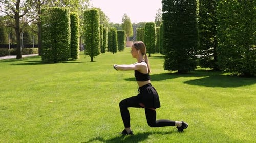 A Woman Doing Fitness She Does Squats with an Expander in a Park in the Morning